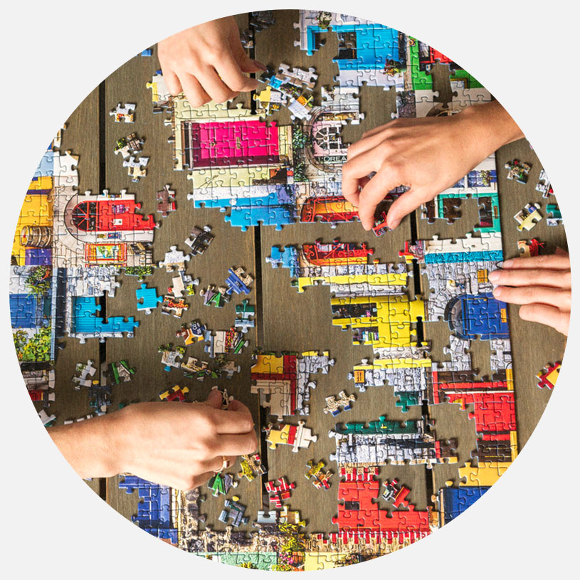 Tre personer samler et farverigt puslespil på et træbord.