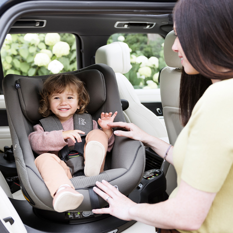 Barn i autostol med voksen der justerer selen.