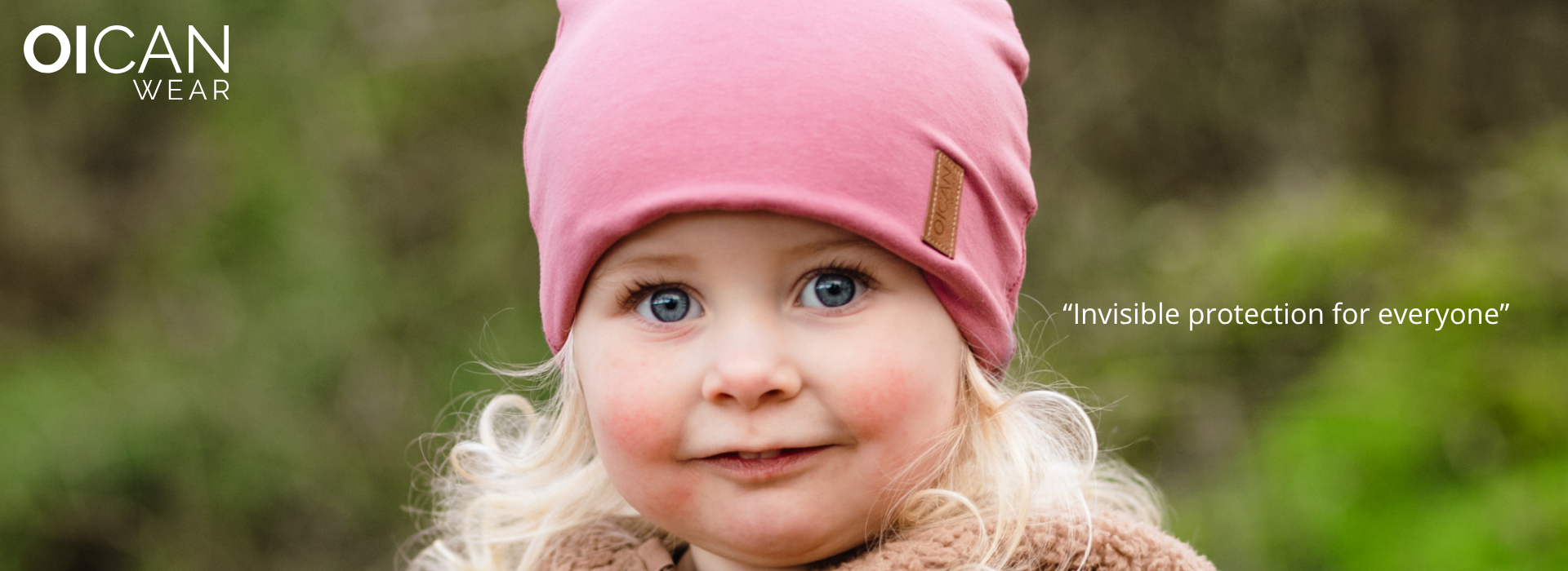 Barn i lyserød hue mod sløret naturbaggrund.