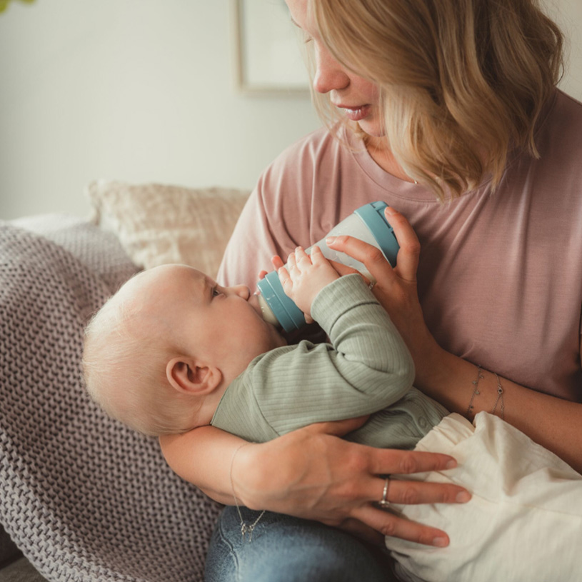 Kvinde fodrer baby med sutteflaske i skødet.