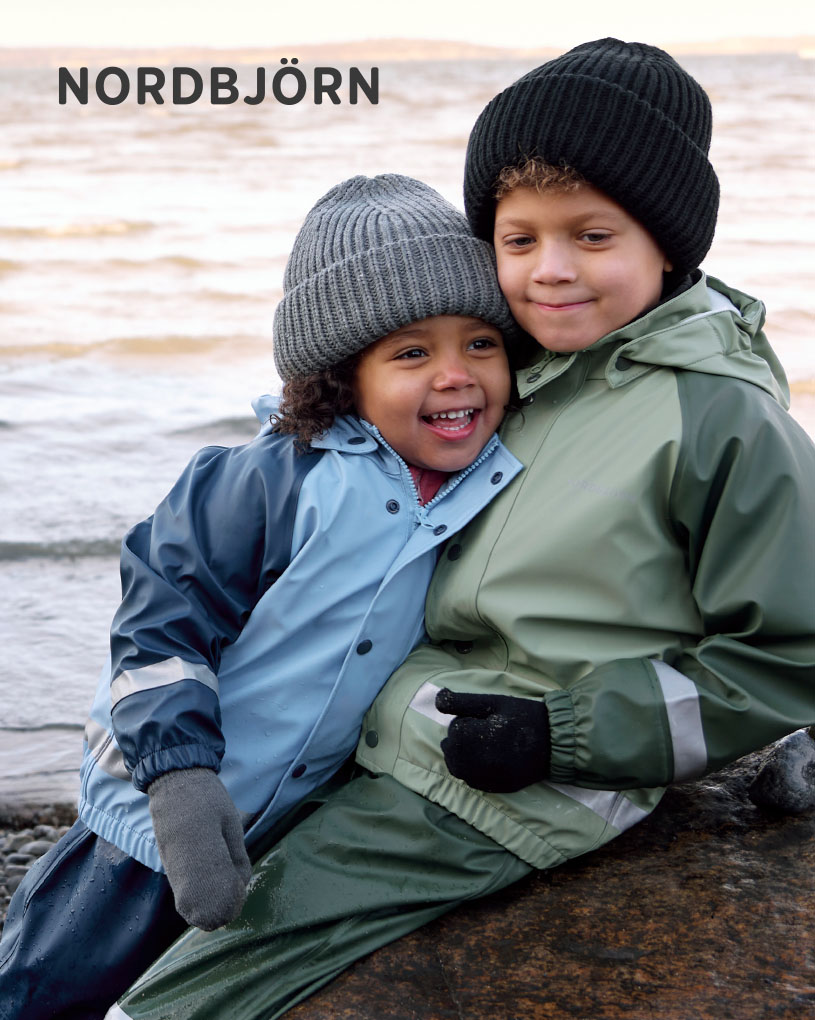Barn i solhat leger med spande på en træterrasse.