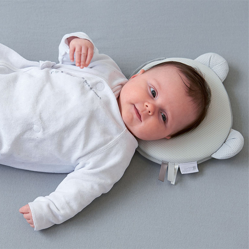 Baby i hvid pyjamas ligger på en pude med bjørneform.