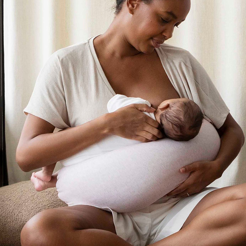 Kvinde ammer spædbarn hvilende på pude.