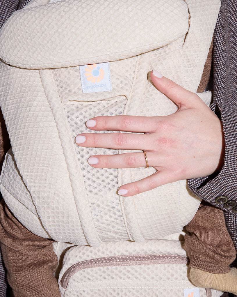 Bærseler i beige med en hånd, der holder fast, og teksten 'ergobaby'.