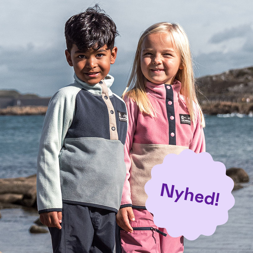 To børn i regntøj holder hænderne på en klippe ved vandet.