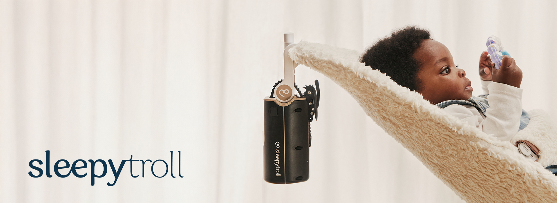 Baby i en babysitter med en legetøj, ved siden af en Sleepytroll-enhed.