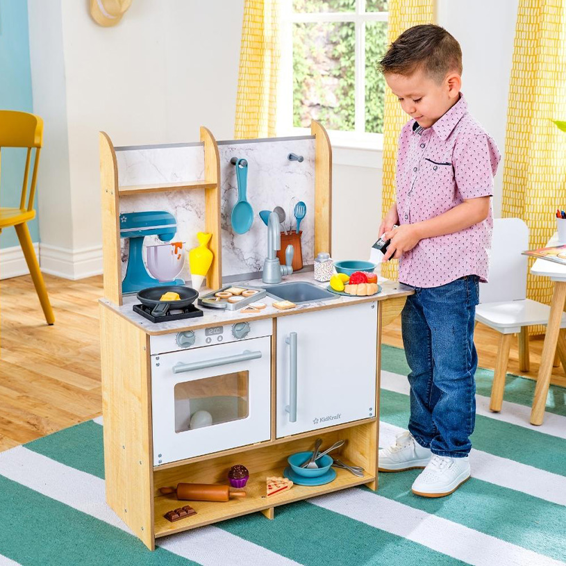 Dreng leger med legetøjskøkken og legetøjsmad i et farverigt rum.