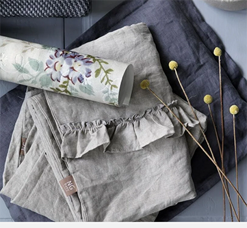 Grå linneduge og blomstrende papir ved siden af tørrede guldfarvede blomster på et bord.