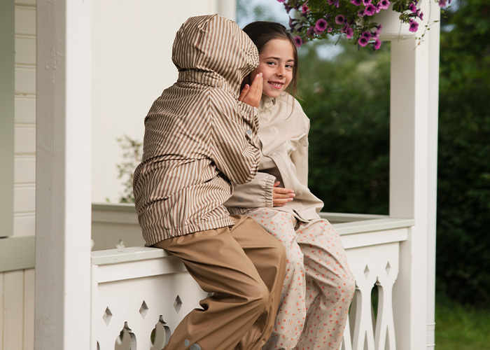 To børn sidder på en balkon og hvisker til hinanden, med teksten 'Kenza X Viking'.