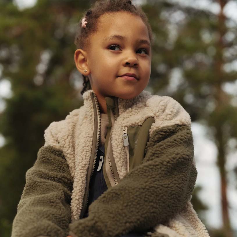 Barn i lyserød jakke smiler til solen.