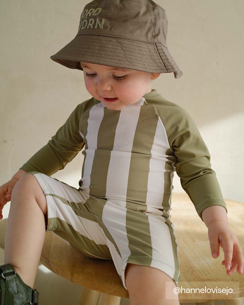 Barn i stribet UV-dragt og solhat sidder indenfor.