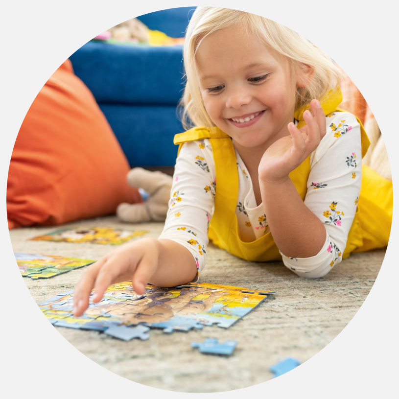 Smilende barn i gult samler puslespil på gulvet.