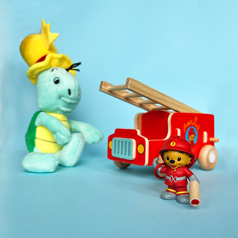Legetøj på blå baggrund: bamse, brandbil og figur i brandmandstøj.