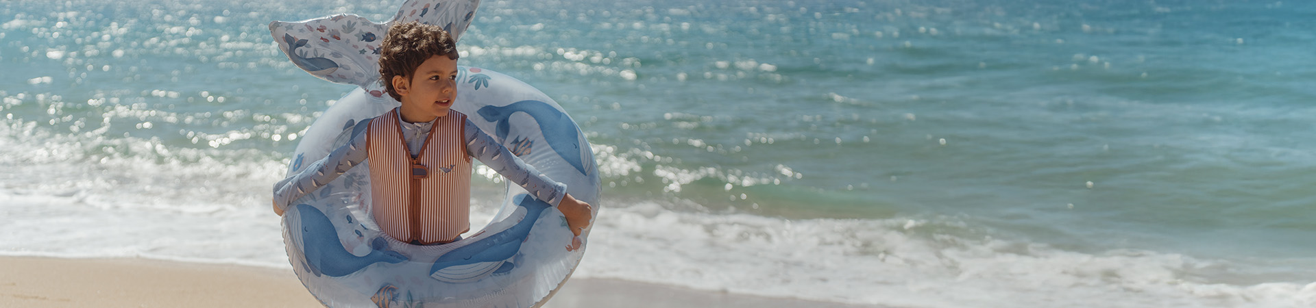 Barn på strand med badering, hav i baggrunden. Tekst: "Nyt for sæsonen".
