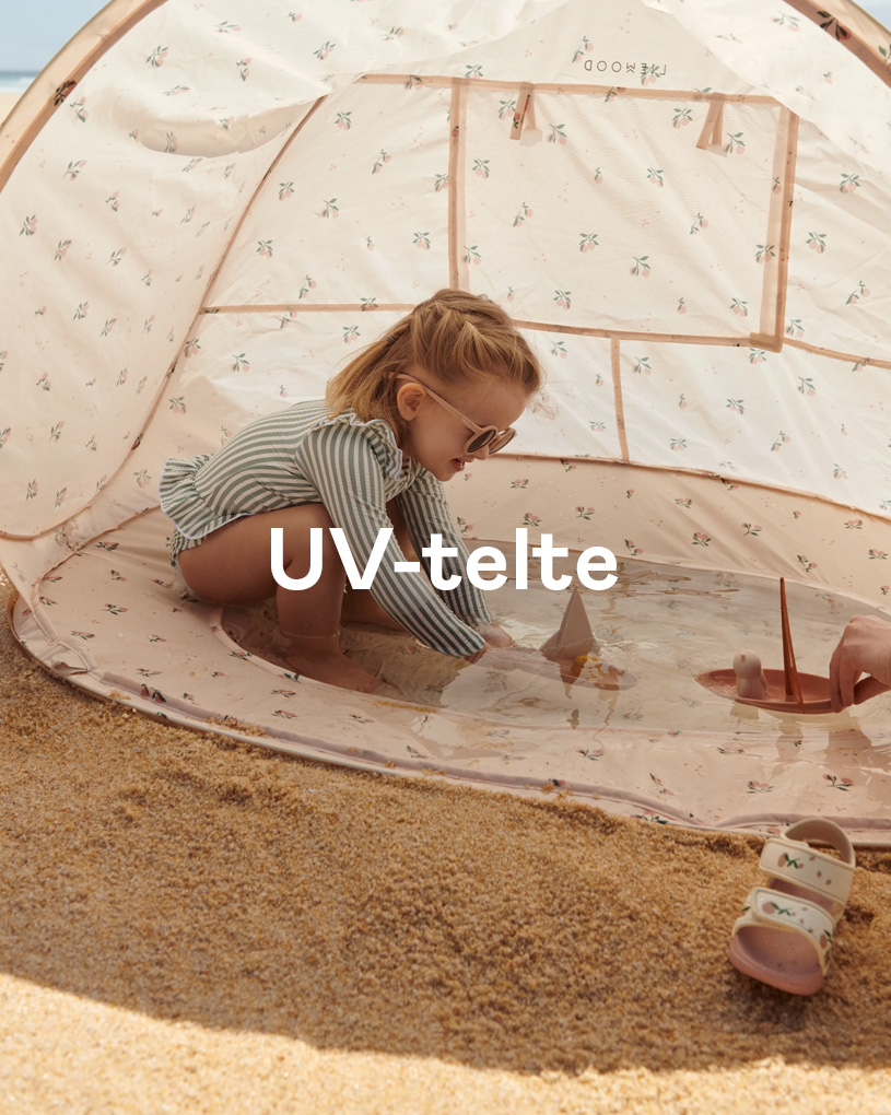 Barn leger i et UV-telt på stranden, omgivet af sol og legetøj.