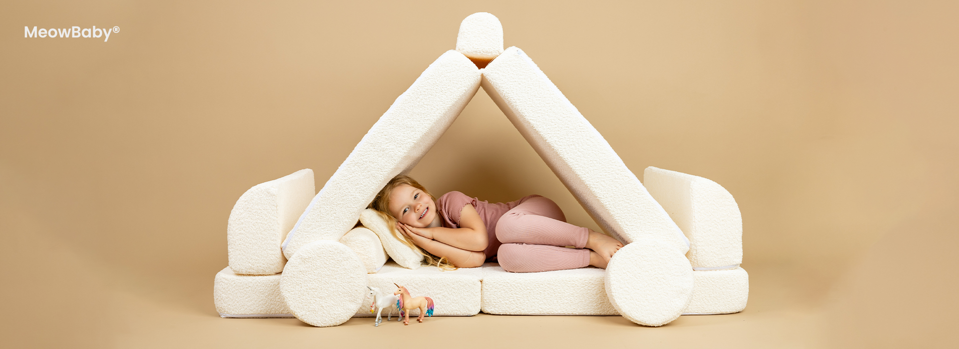 Barn i lyserødt tøj ligger på hvide puder formet som et hus.