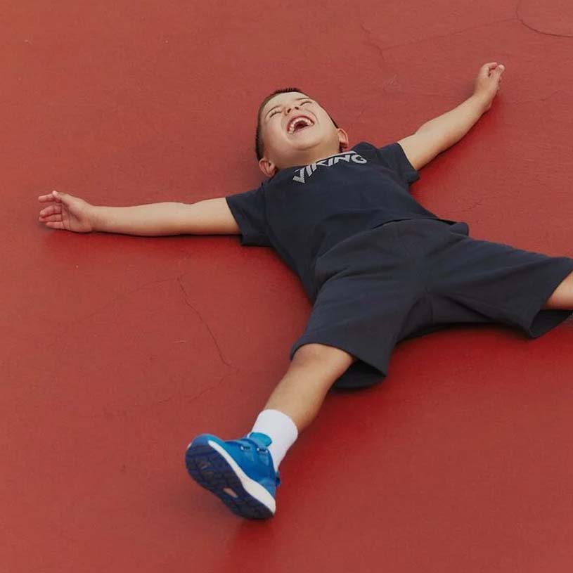 Barn i blå hættetrøje og shorts leger på rød flade.