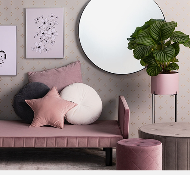 Lyserød sofa med puder, rund spejl og plante i krukke.