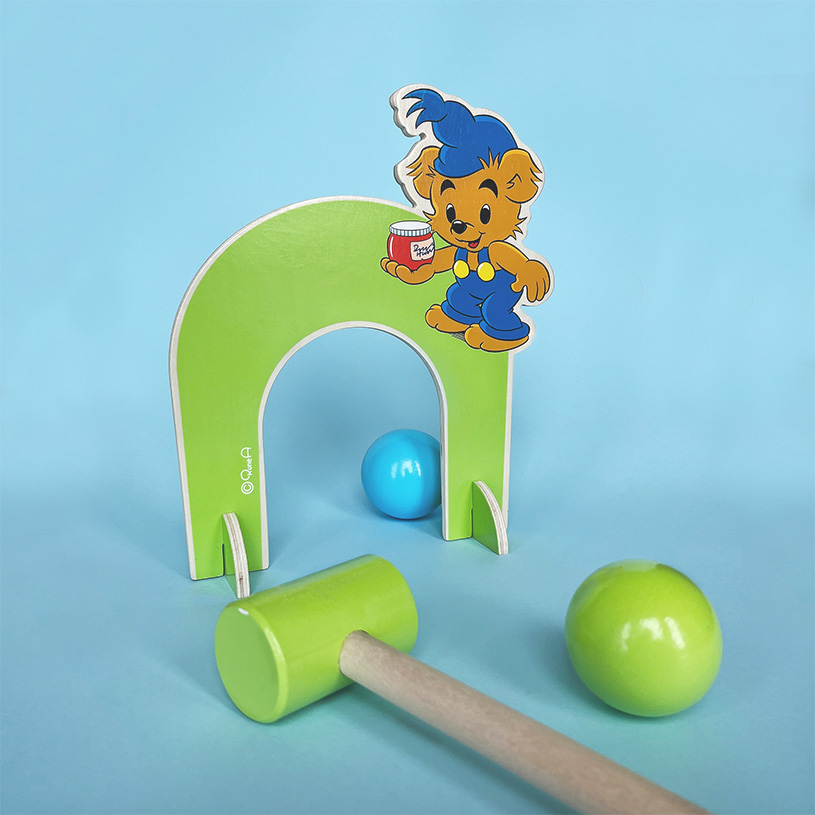 Legetøj med bamsefigur, grønt forhindring og kølle på blå baggrund.