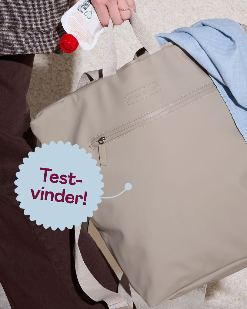 En person holder en beige skötväska med teksten 'Bedst i test'.