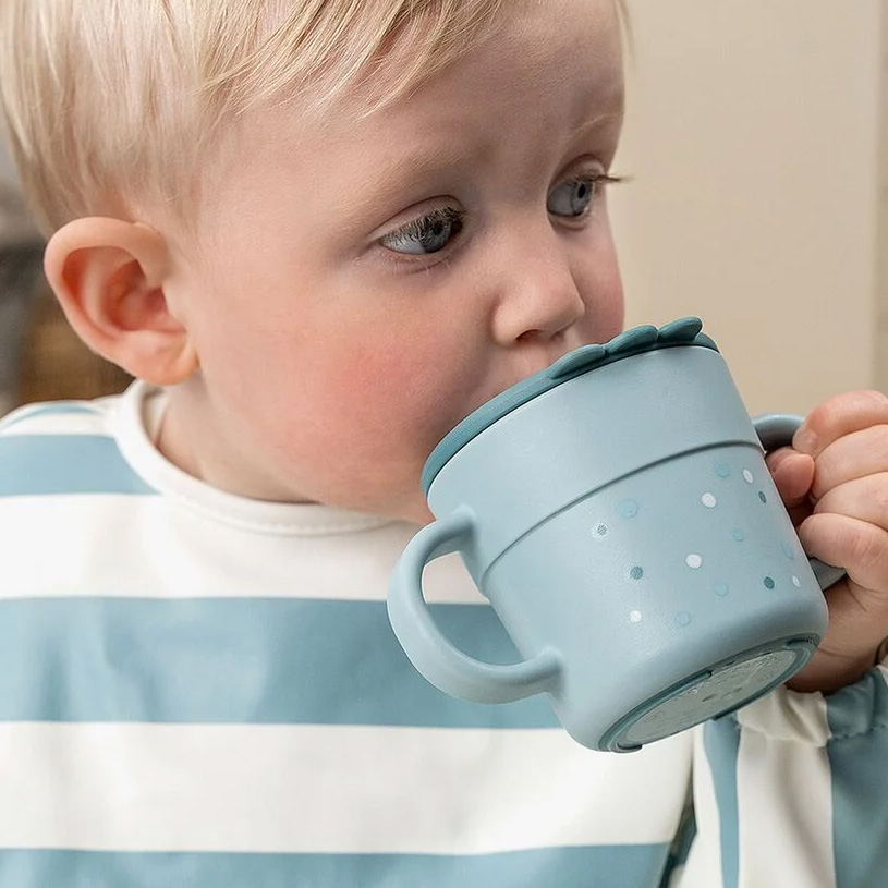 Baby drikker rød drik fra kop.