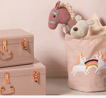 Lyserød kurv med tøjdyr og enhjørninger ved siden af lyserøde kasser.