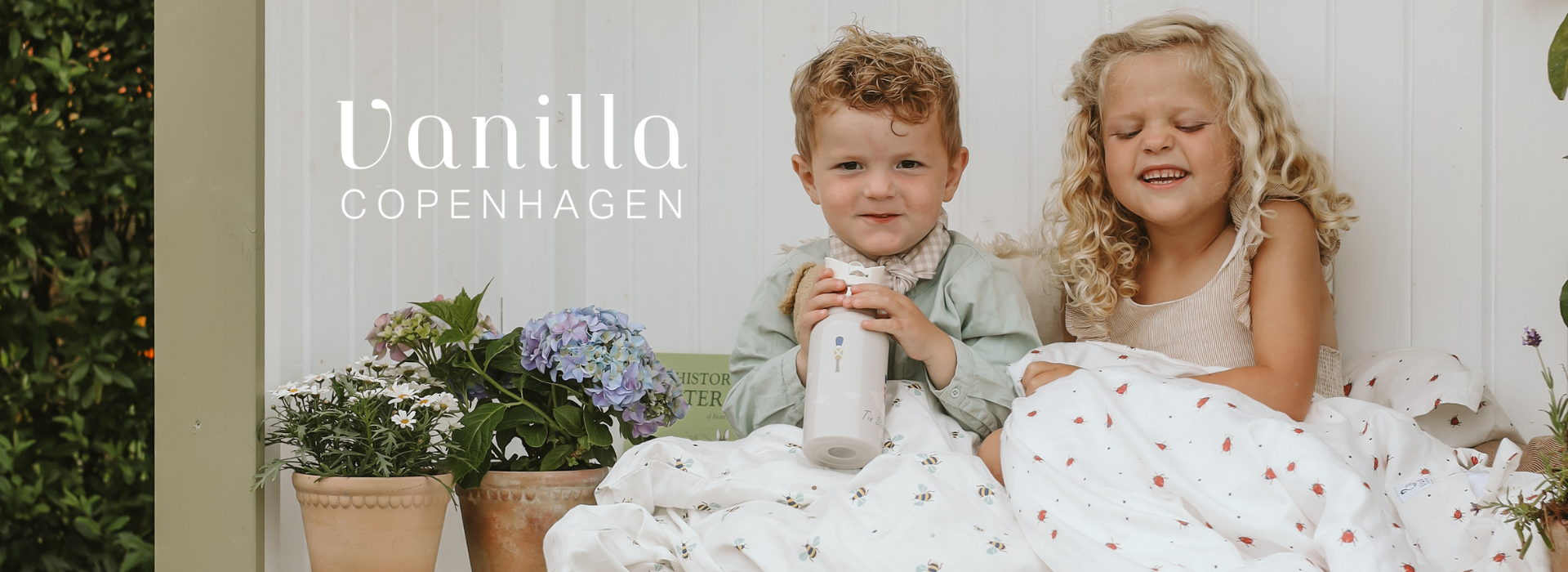 To børn sidder med et tæppe udenfor ved siden af blomster.