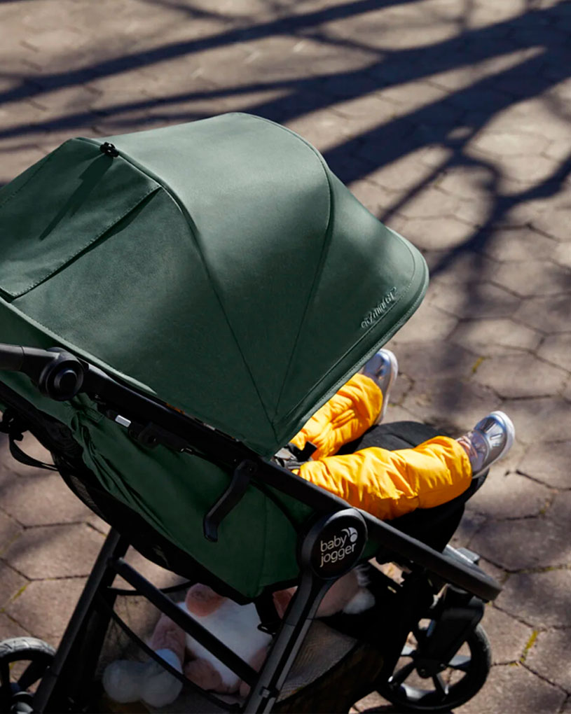 Barnevogn med grønt tag og barn i gule bukser.