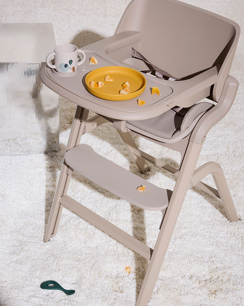 Højstol med en gul tallerken og en kop, der indeholder stykker af appelsin.