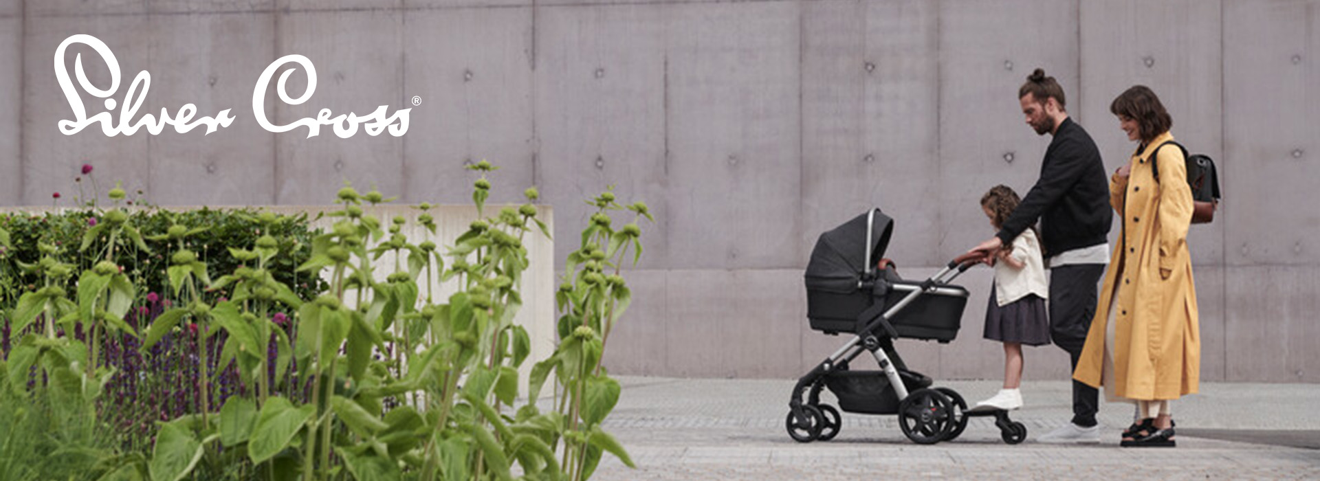 Familie med barnevogn går ved betonvæg og have.