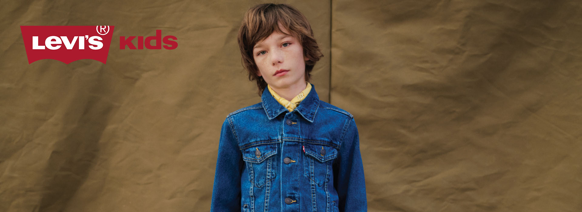 Barn i en denimjakke foran brun baggrund.