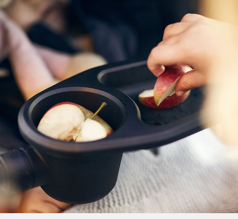 Et barn tager æblestykker fra en klapvognsbakke.